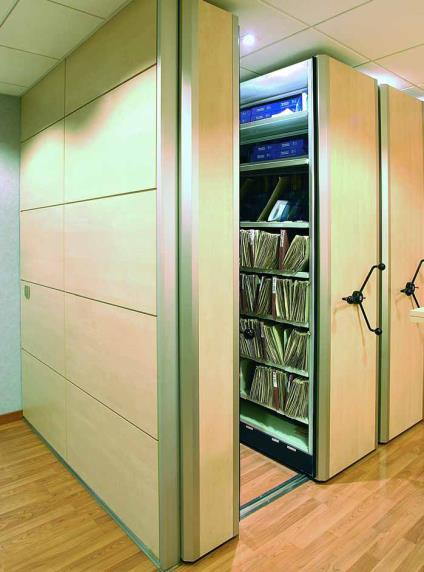 Estantería móvil de archivo con bases sobre rieles y manivela de desplazamiento, mostrando un módulo abierto con documentos almacenados